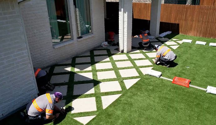 A professional team installing synthetic green grass around a high-end residential backyard